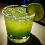 A vibrant, bright green Fresh Jalapeño Lime Margarita served over ice with a salt rim and lime wheel garnish.