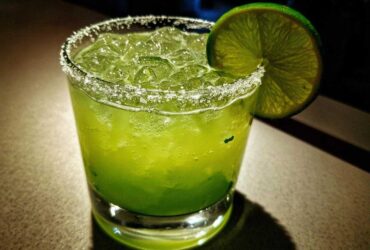 A vibrant, bright green Fresh Jalapeño Lime Margarita served over ice with a salt rim and lime wheel garnish.