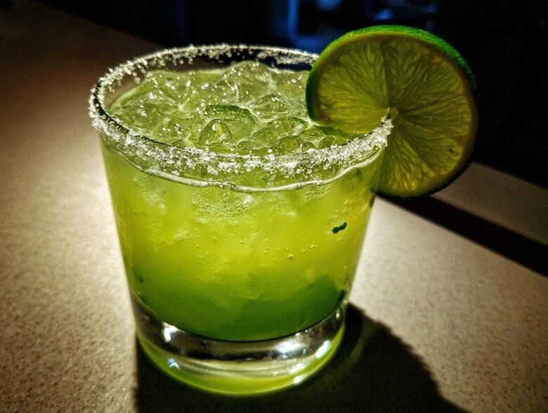 A vibrant, bright green Fresh Jalapeño Lime Margarita served over ice with a salt rim and lime wheel garnish.