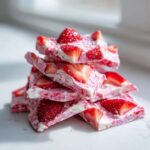A stack of bright pink and white Frozen Strawberry Yogurt Bark pieces topped with fresh strawberry slices.