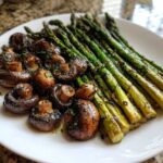 A white plate featuring perfectly cooked Garlic Butter Roasted Asparagus and mushrooms, glistening with butter and herbs.