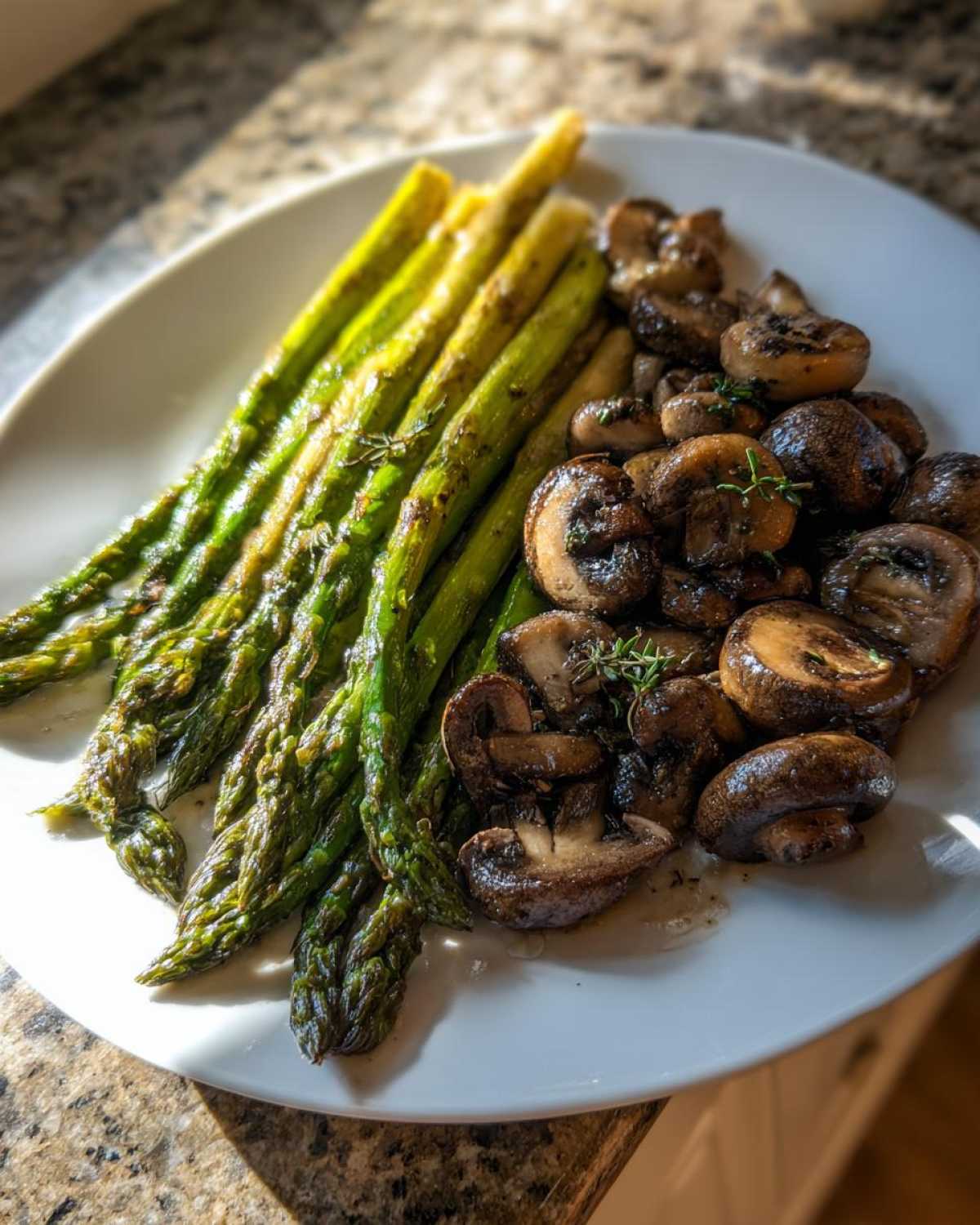 A white plate featuring roasted asparagus spears and sautéed mushrooms seasoned with herbs, highlighting Garlic Butter Roasted Asparagus and Mushrooms.