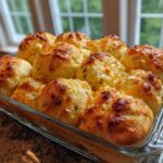 Freshly baked Garlic Parmesan Pull-Apart Bread rolls with browned cheese topping in a clear glass baking dish.