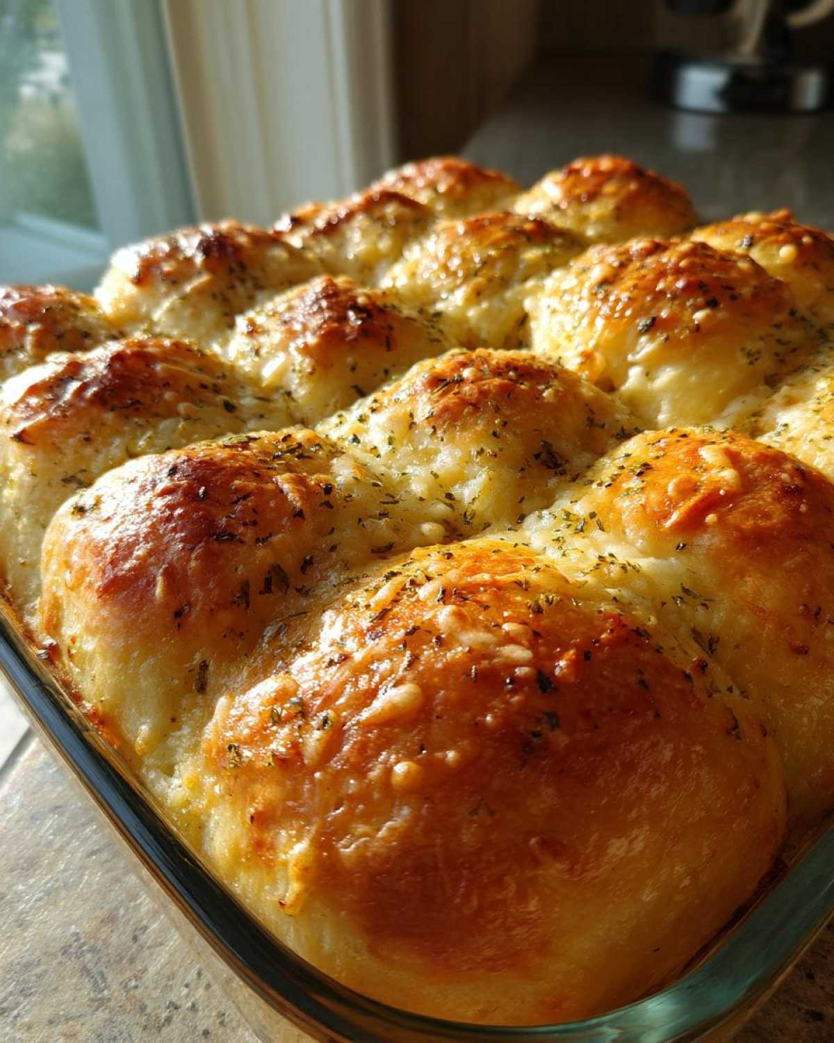 Close-up of freshly baked Garlic Parmesan Pull-Apart Bread with melted cheese and herbs in a glass baking dish.