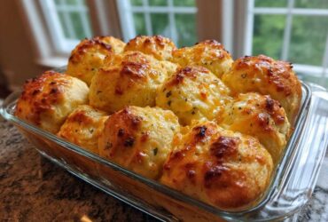 Freshly baked Garlic Parmesan Pull-Apart Bread rolls with browned cheese topping in a clear glass baking dish.