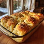 Golden brown Garlic Parmesan Pull-Apart Bread baked in a clear glass dish, topped with melted cheese and herbs.