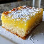 A close-up of a single serving of Gluten-Free Lemon Bars with a bright yellow filling and shortbread crust, dusted with powdered sugar.
