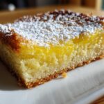 A close-up of a single serving of Gluten-Free Lemon Bars, showing the bright yellow filling and shortbread crust, dusted with powdered sugar.