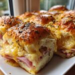 Close-up of baked Hawaiian Roll Ham and Cheese Sliders oozing melted cheese and topped with herbs.