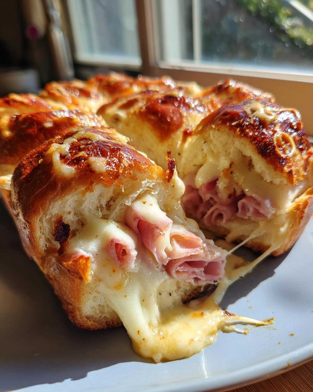 Close-up of Hawaiian Roll Ham and Cheese Sliders with melted cheese stretching as one is pulled apart.
