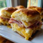 Close-up of baked Hawaiian Roll Ham and Cheese Sliders dripping with honey mustard glaze on a white plate.