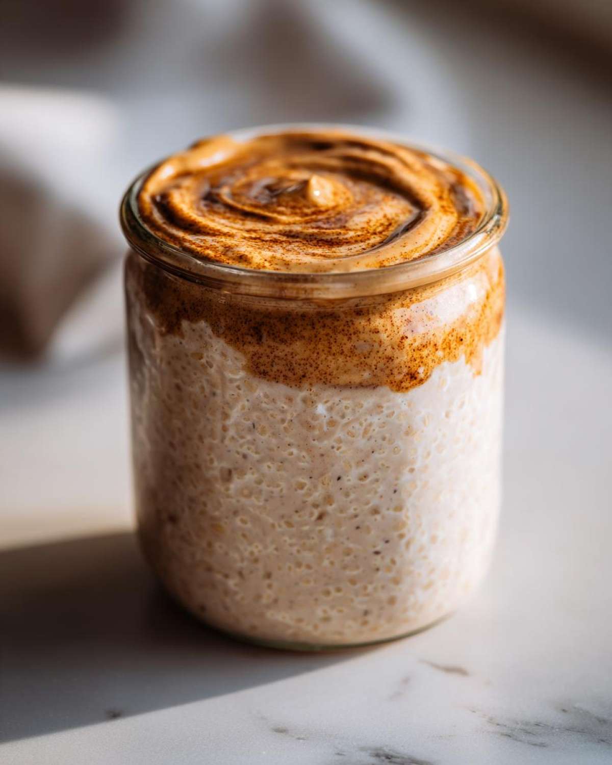 A jar filled with creamy High-Protein Peanut Butter Overnight Oats topped with a swirl of peanut butter cream and cinnamon.