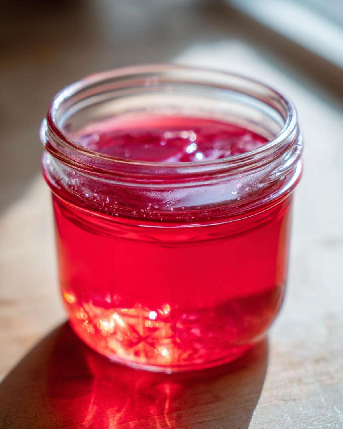 Close-up of bright red Homemade Strawberry Lemonade Concentrate stored in a small glass jar.