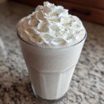 A tall glass of Homemade Vanilla Bean Frappuccino topped with whipped cream and vanilla bean specks.