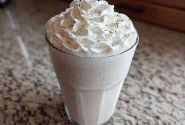 A tall glass of Homemade Vanilla Bean Frappuccino topped with whipped cream and vanilla bean specks.