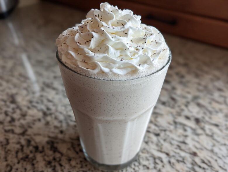 A tall glass of Homemade Vanilla Bean Frappuccino topped with whipped cream and vanilla bean specks.