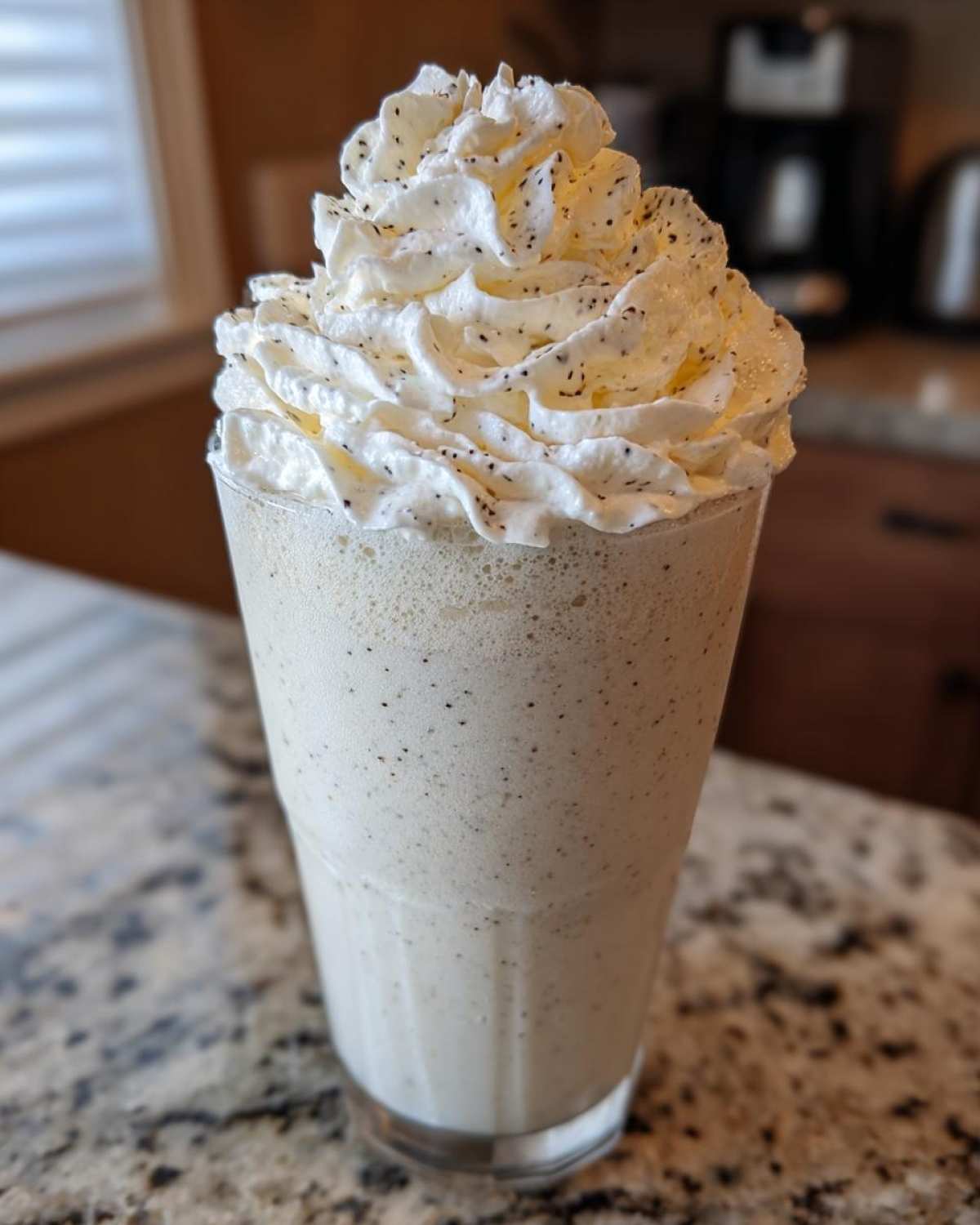 A tall glass of Homemade Vanilla Bean Frappuccino topped with vanilla bean speckled whipped cream.