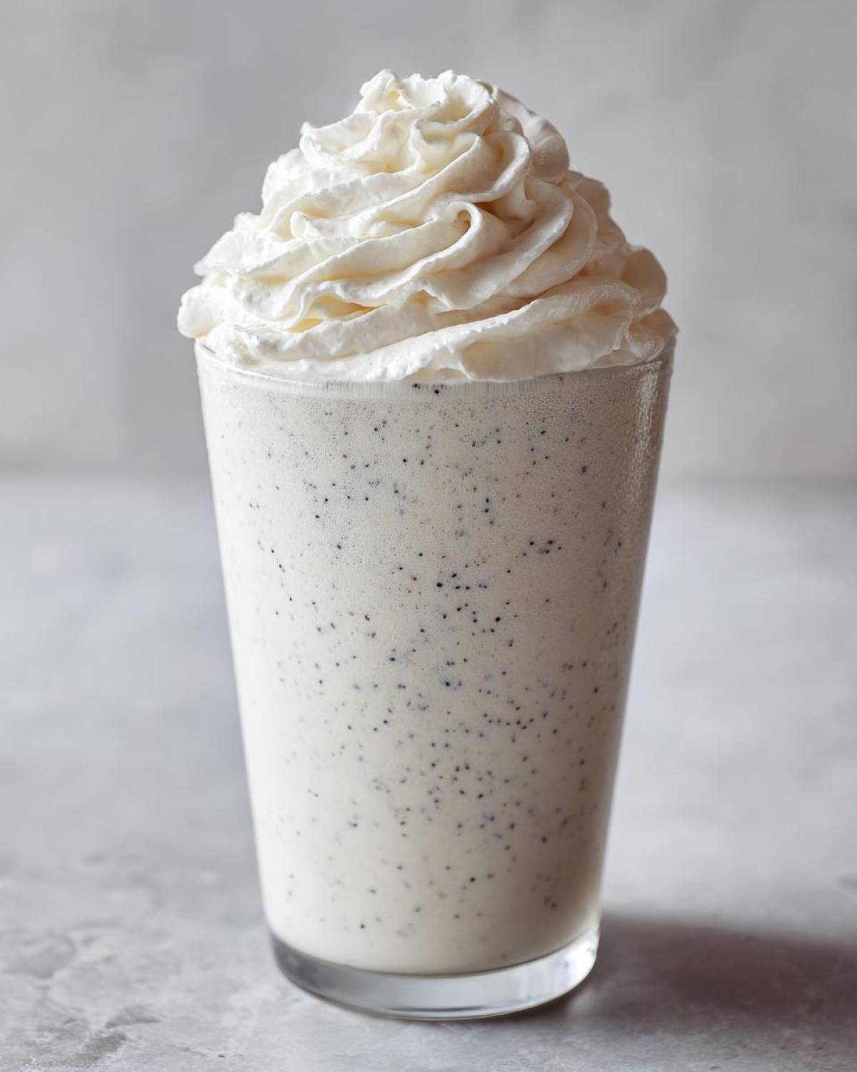A tall glass of Homemade Vanilla Bean Frappuccino topped with a swirl of whipped cream.