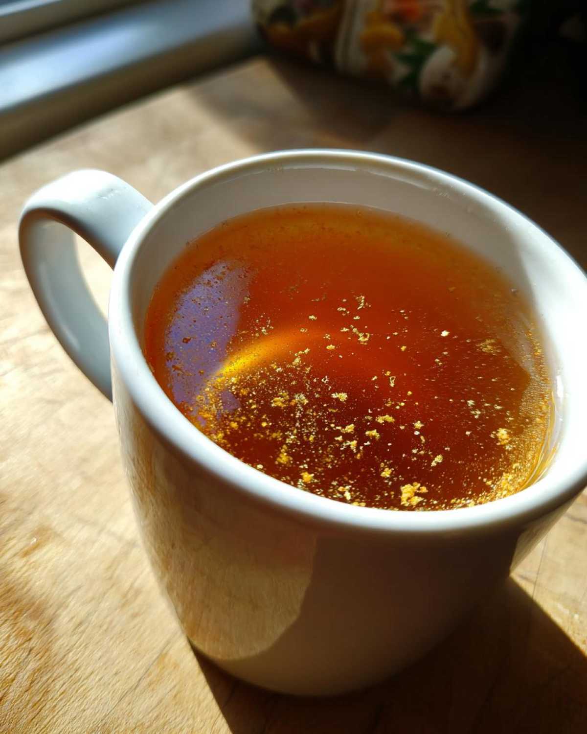 Close-up of warm Honey Lemon Ginger Tea in a white mug, showing ginger particles floating on the surface.