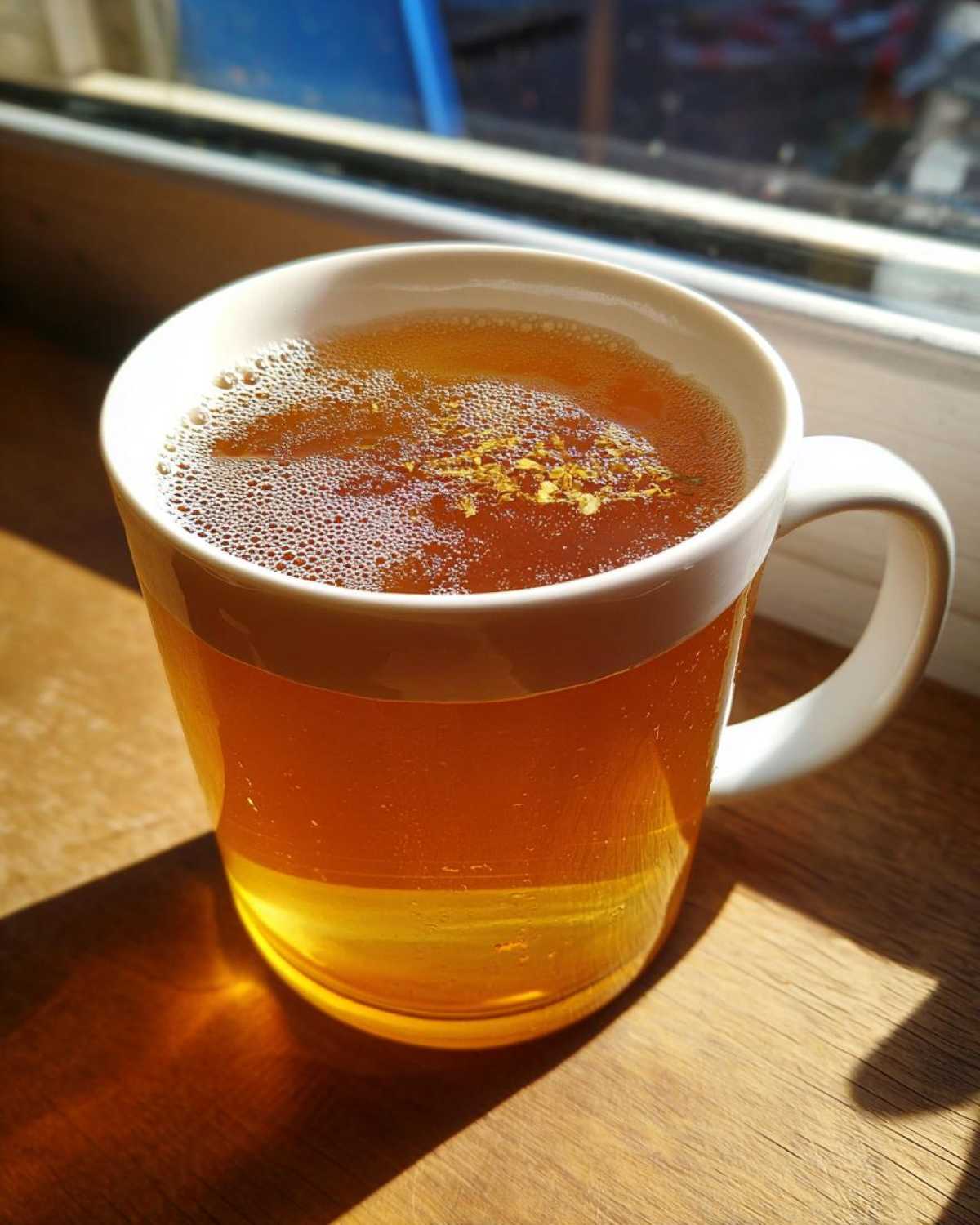 A warm mug of Honey Lemon Ginger Tea with visible ginger pieces floating on top, backlit by sunlight.