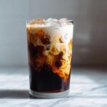 Close-up of an Iced Honey Almond Milk Latte showing the creamy almond milk swirling into the dark espresso.