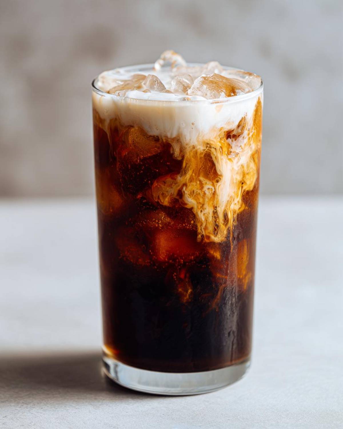 A tall glass filled with an Iced Honey Almond Milk Latte, showing dark coffee swirling with creamy almond milk and topped with ice.