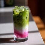 A tall glass showing layers of bright pink strawberry syrup, white milk, and vibrant green matcha in an Iced Strawberry Matcha Latte.