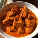 Close-up of creamy, orange Instant Pot Butter Chicken pieces garnished with dried herbs in a white bowl.