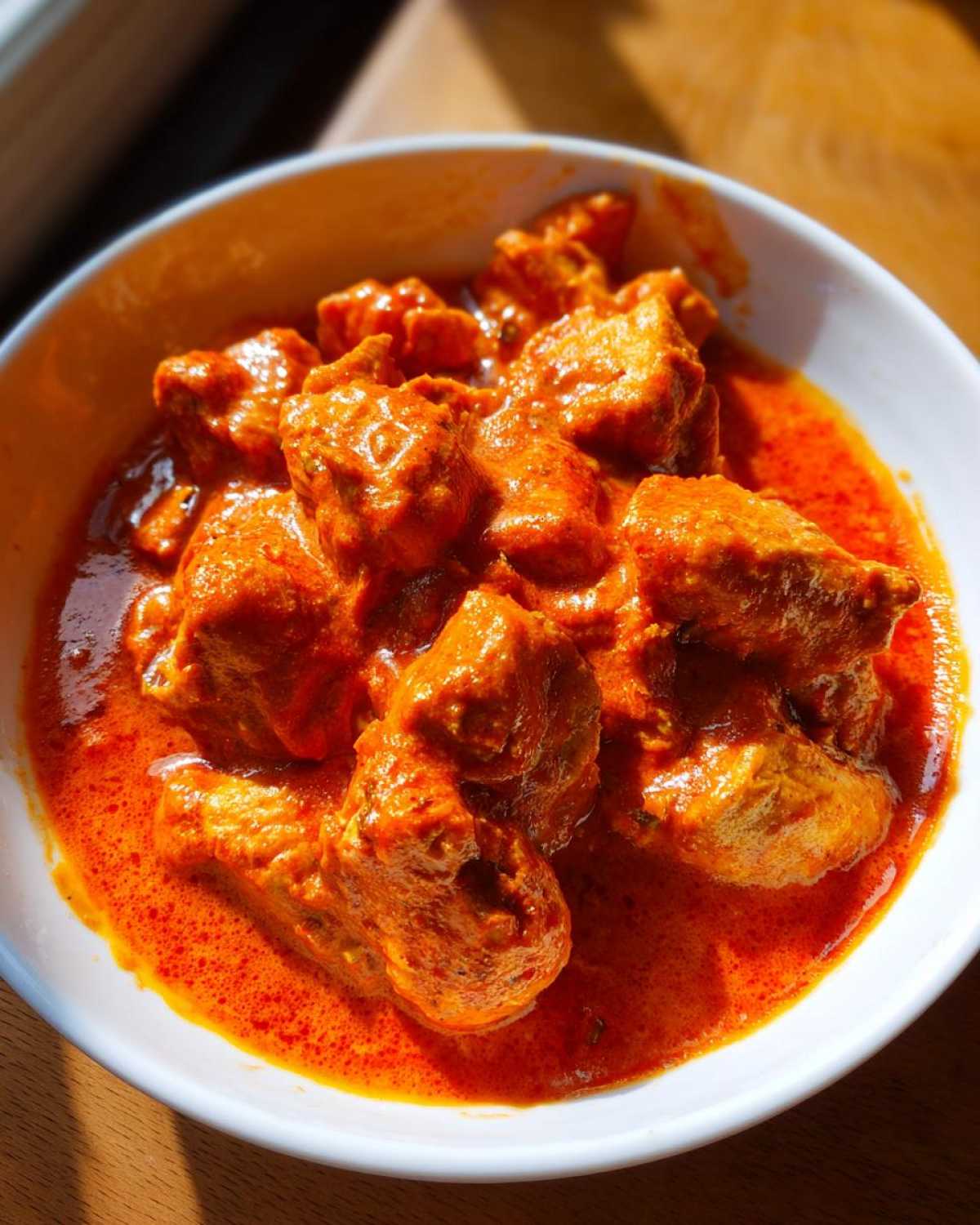 Close-up of rich, vibrant orange Instant Pot Butter Chicken pieces submerged in creamy sauce in a white bowl.