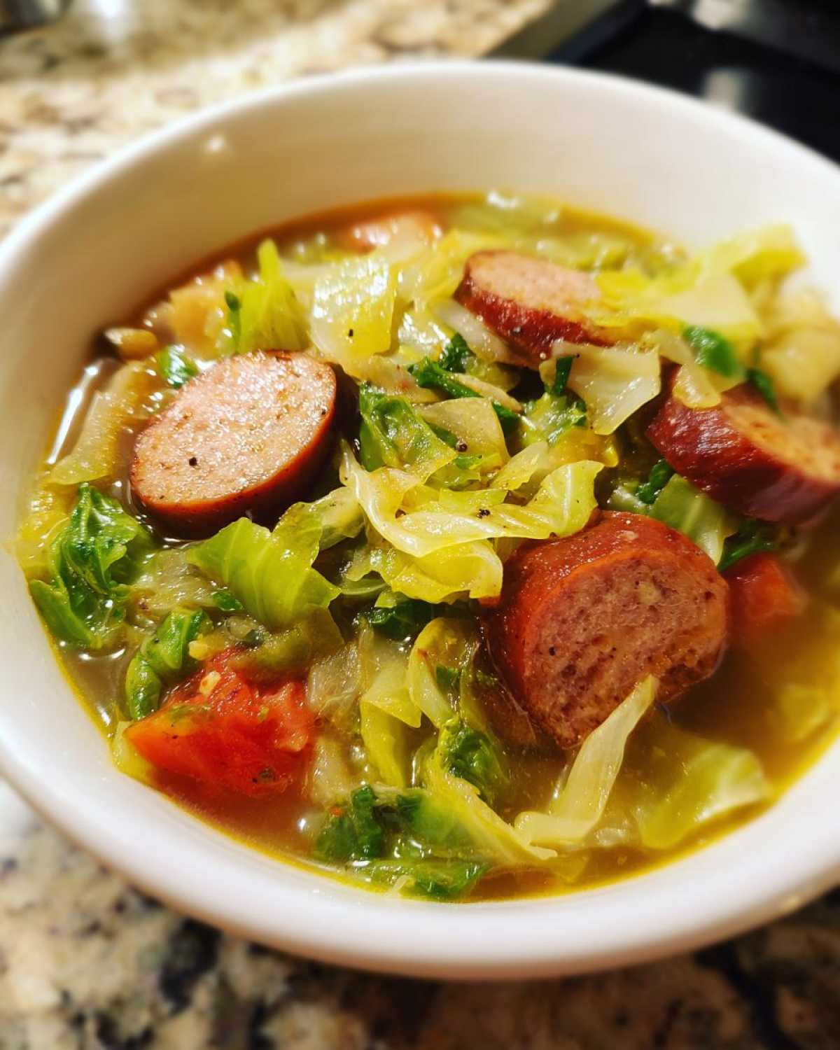 Close-up of a white bowl filled with Instant Pot Cabbage and Sausage Soup, featuring sliced sausage and bright green cabbage.
