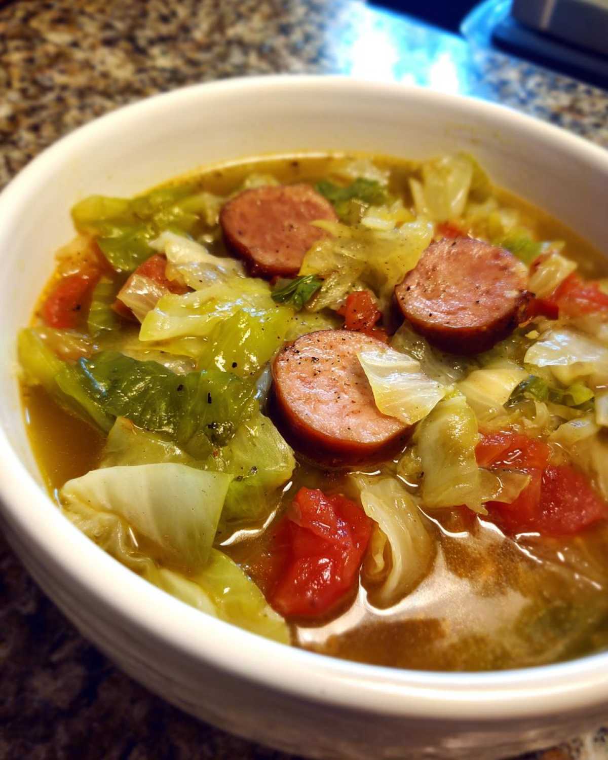 Close-up of a white bowl filled with Instant Pot Cabbage and Sausage Soup, featuring chunks of sausage, cabbage, and tomatoes.