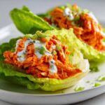 Two servings of vibrant Keto Buffalo Chicken Lettuce Wraps piled high with orange shredded chicken, ranch dressing, and green onions.