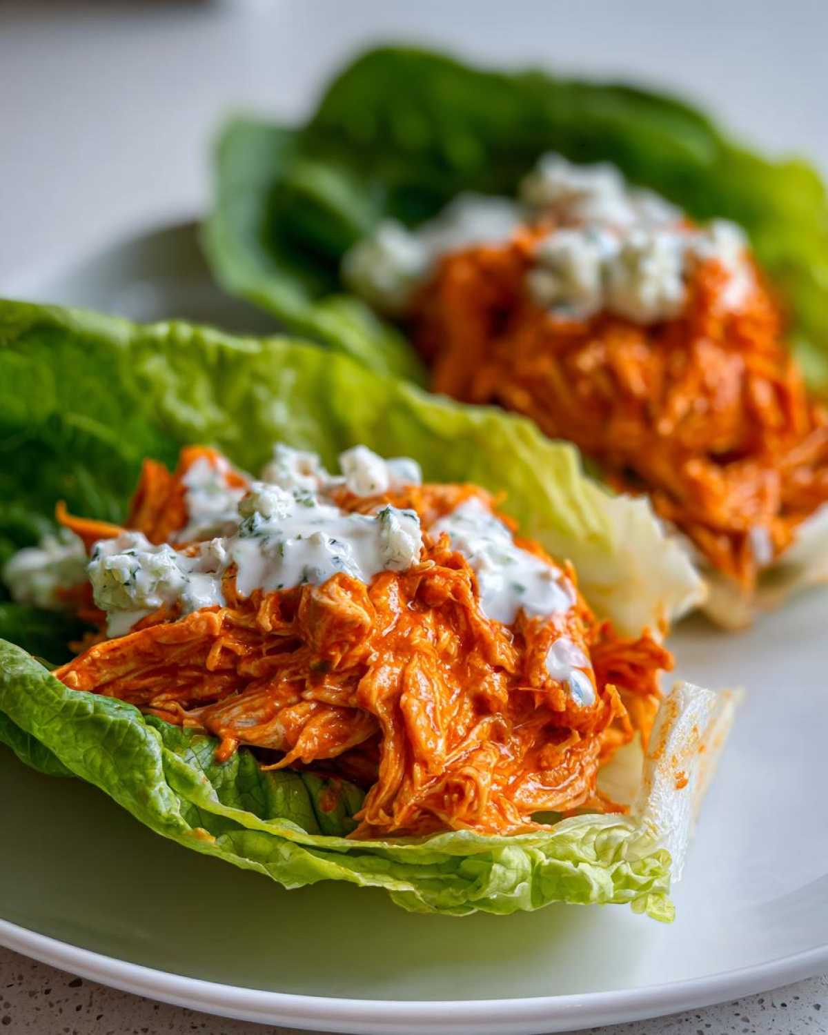 Two servings of Keto Buffalo Chicken Lettuce Wraps featuring shredded orange buffalo chicken topped with blue cheese dressing.