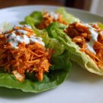 Three servings of Keto Buffalo Chicken Lettuce Wraps filled with shredded orange chicken and topped with a drizzle of white ranch dressing.