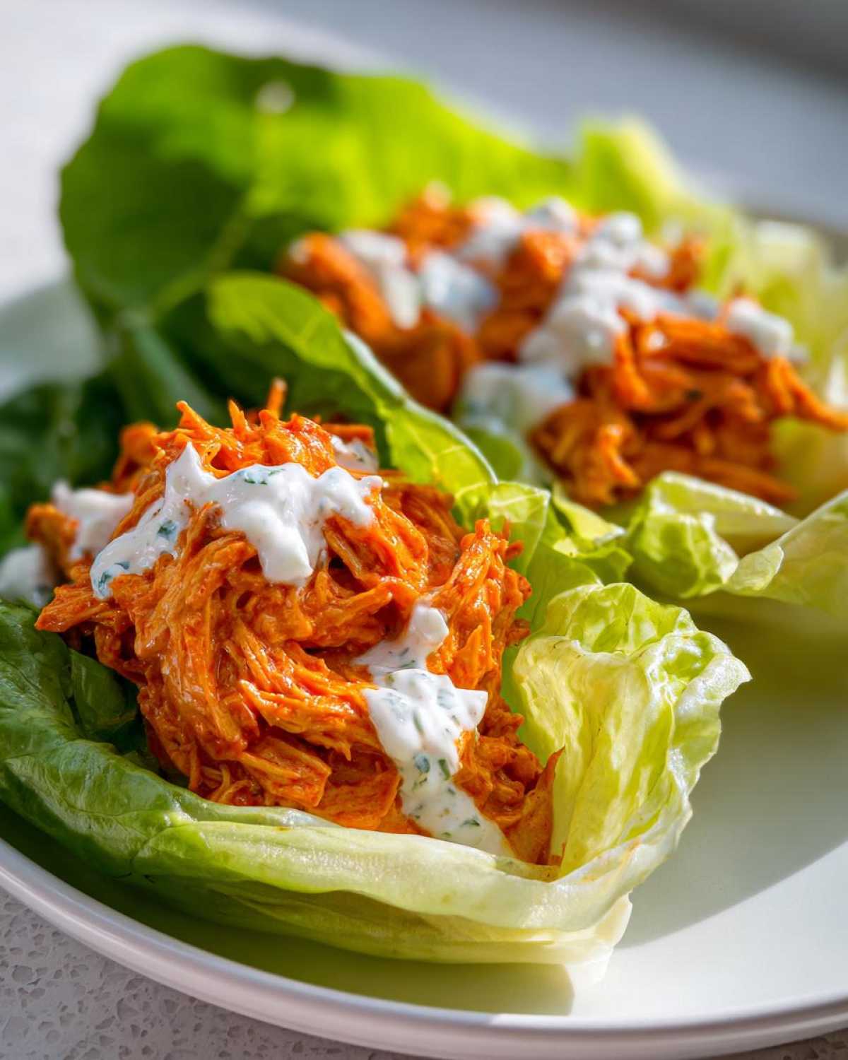 Two Keto Buffalo Chicken Lettuce Wraps filled with orange shredded chicken and topped with a drizzle of ranch or blue cheese dressing.