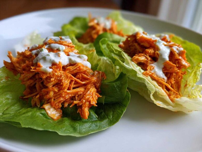 Three servings of Keto Buffalo Chicken Lettuce Wraps filled with shredded orange chicken and topped with a drizzle of white ranch dressing.