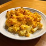 A close-up of a serving of rich, cheesy Keto Cauliflower Mac and Cheese on a white plate.