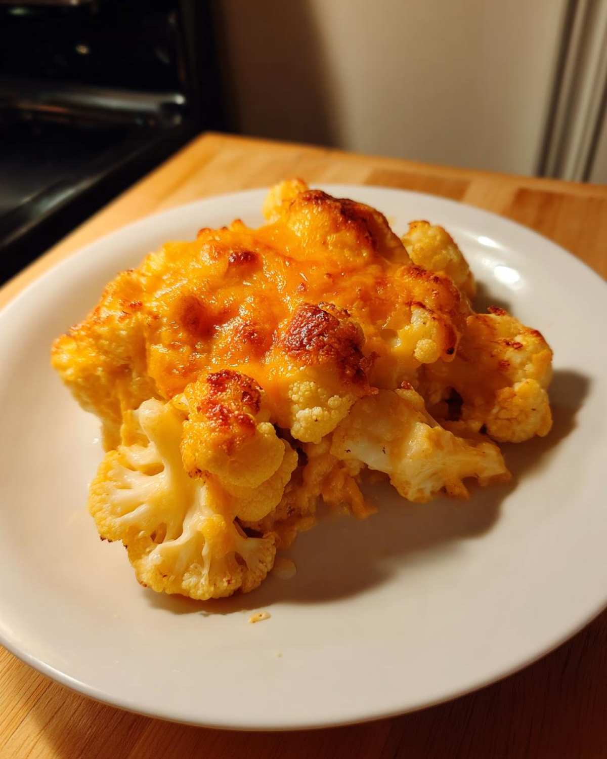 A serving of Keto Cauliflower Mac and Cheese on a white plate, featuring tender cauliflower florets covered in melted, browned cheddar cheese.