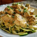 A close-up of Keto Chicken Alfredo featuring creamy sauce-covered chicken pieces served over bright green zucchini noodles (zoodles).