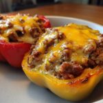 Two halves of Keto Taco Stuffed Peppers, one red and one yellow, topped with seasoned ground meat and melted cheddar cheese.