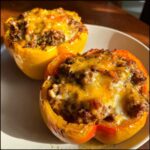Two baked yellow bell peppers filled with seasoned ground meat and topped with melted cheddar cheese, ready to eat as Keto Taco Stuffed Peppers.