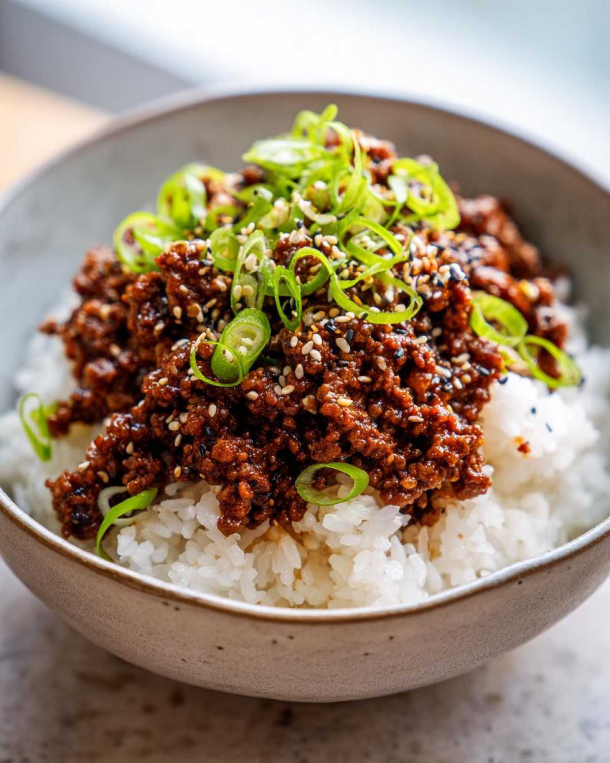 A close-up of Korean Ground Beef Bulgogi Bowls featuring savory ground beef over white rice, topped with green onions and sesame seeds.