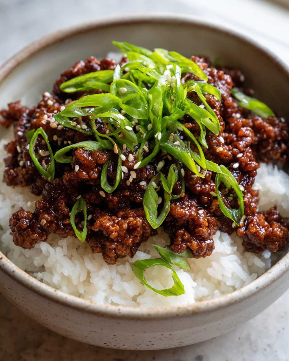 Close-up of a bowl of Korean Ground Beef Bulgogi Bowls served over white rice and garnished with sliced green onions and sesame seeds.