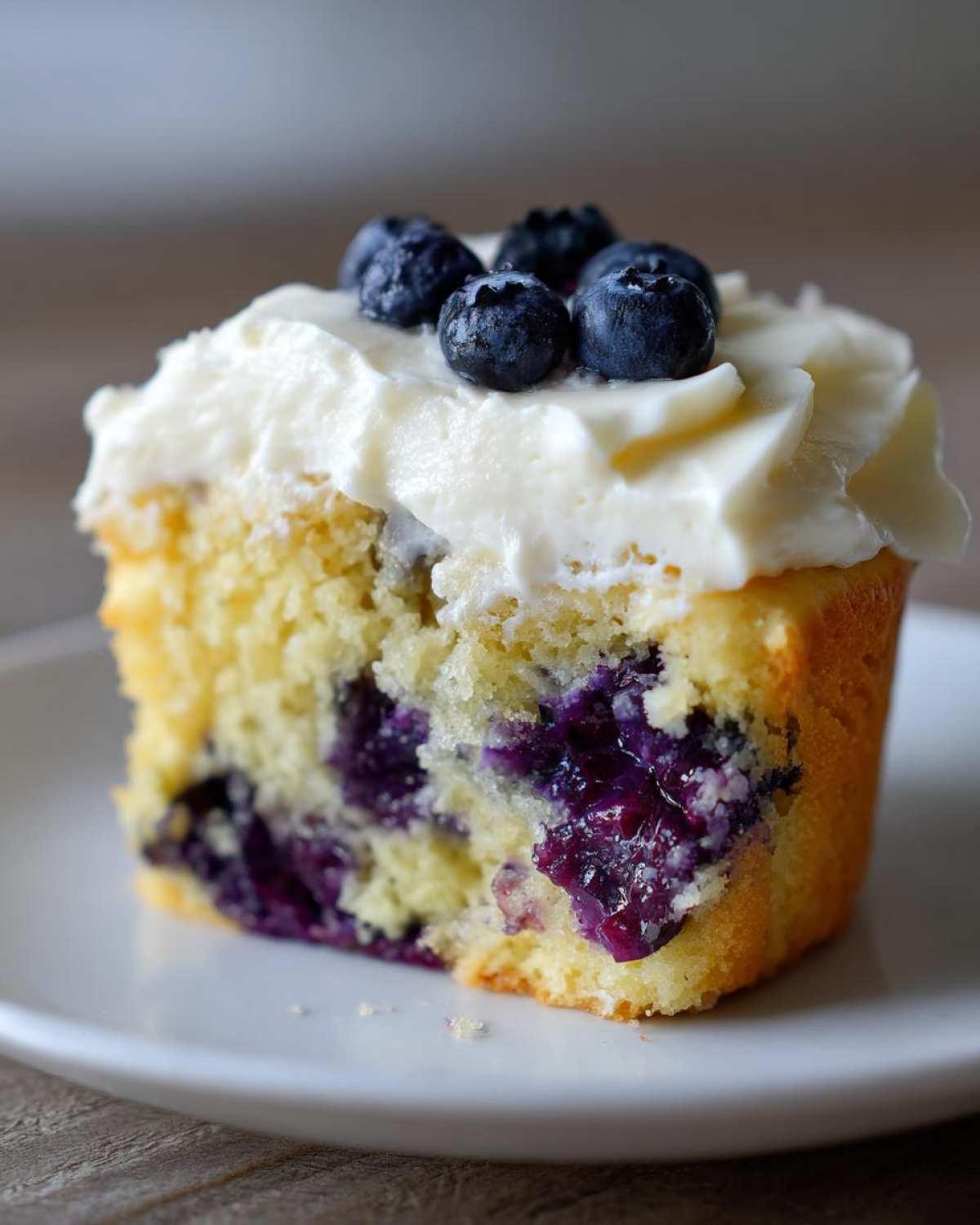 A close-up view of a Lemon Blueberry Cupcakes with Cream Cheese Frosting, showing the moist crumb and fresh blueberries.