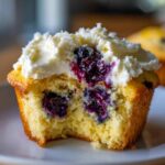 Close-up of a Lemon Blueberry Cupcake with cream cheese frosting, showing a bite taken out revealing moist cake and juicy blueberries.