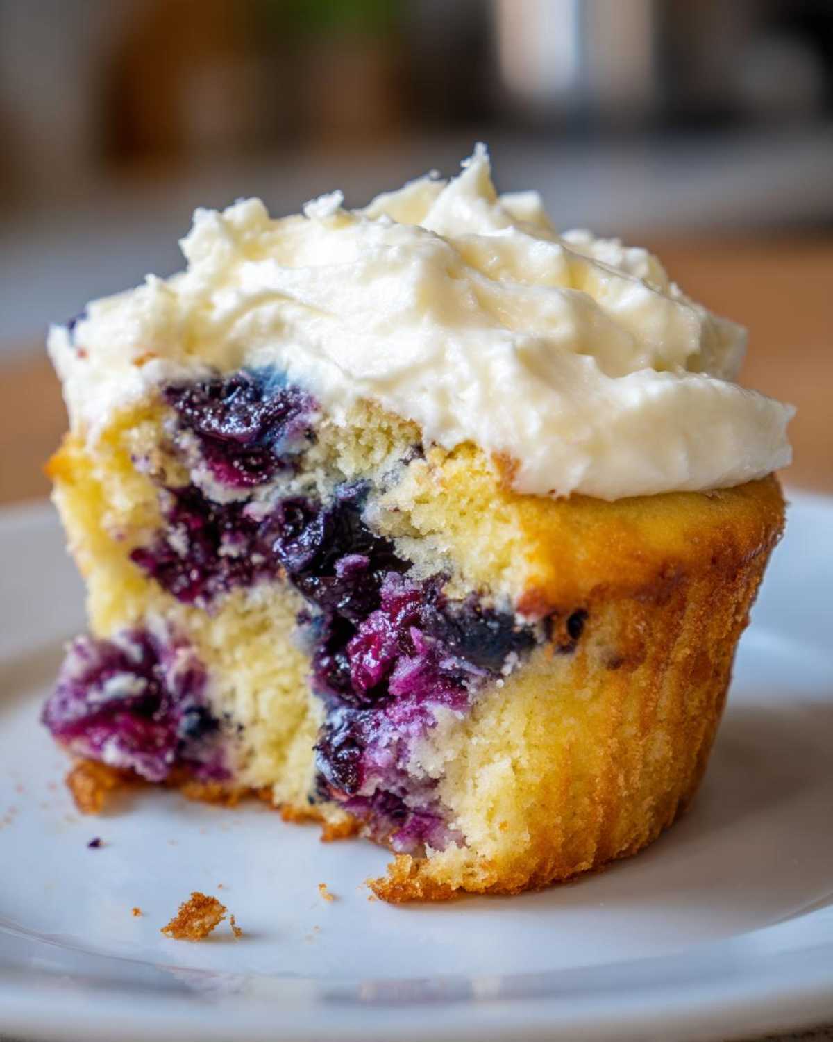 Close-up of a Lemon Blueberry Cupcake with Cream Cheese Frosting, showing the moist interior filled with burst blueberries.