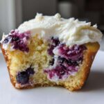Close-up of a Lemon Blueberry Cupcakes with Cream Cheese Frosting, showing the moist crumb and burst blueberries.