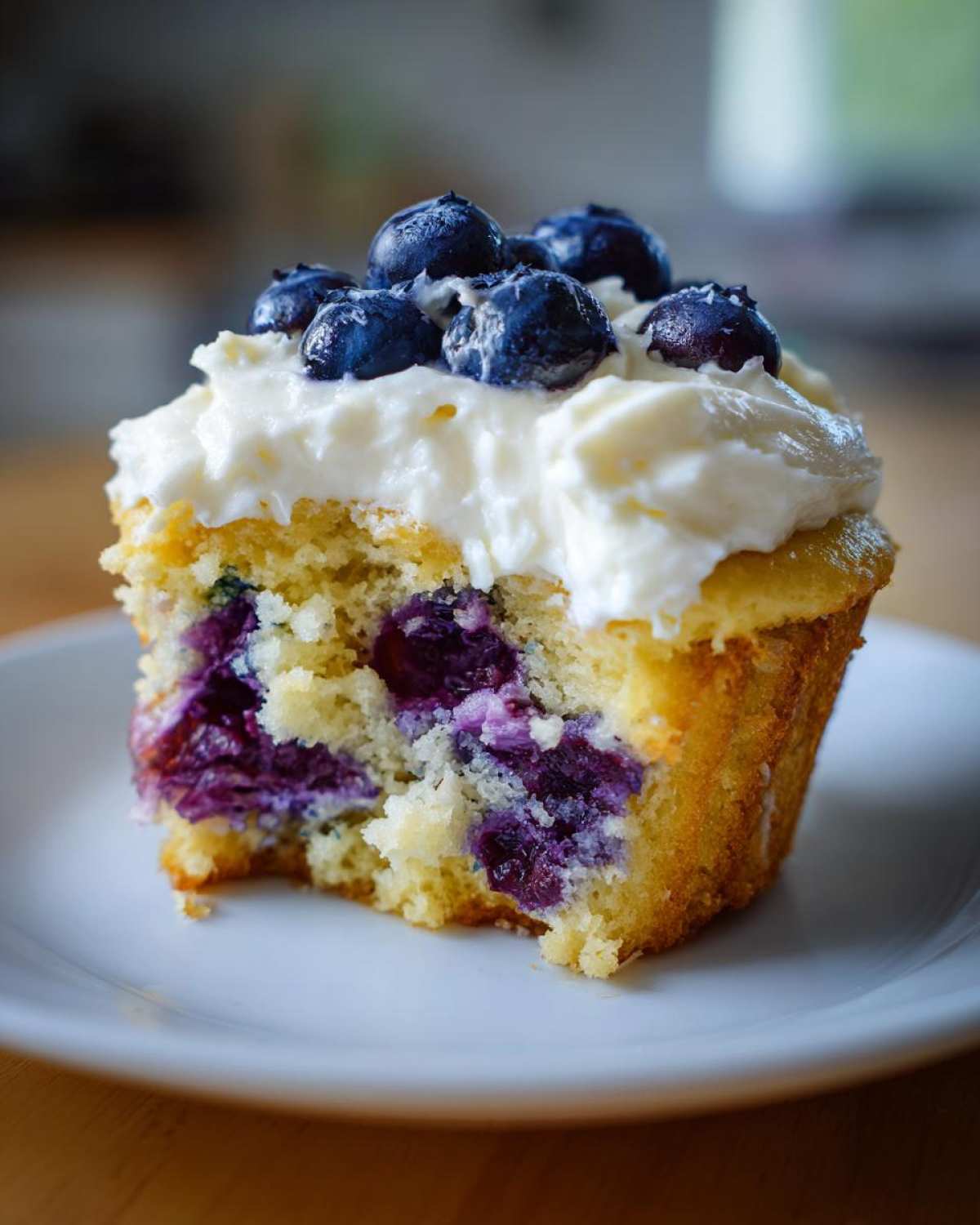 Close-up of a Lemon Blueberry Cupcakes with cream cheese frosting, showing the moist interior filled with purple blueberries.