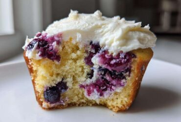 Close-up of a Lemon Blueberry Cupcakes with Cream Cheese Frosting, showing the moist crumb and burst blueberries.