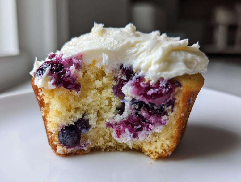 Close-up of a Lemon Blueberry Cupcakes with Cream Cheese Frosting, showing the moist crumb and burst blueberries.